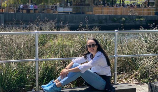 Gizla Maciel sitting on a bench outdoors with tall grasses in the background.