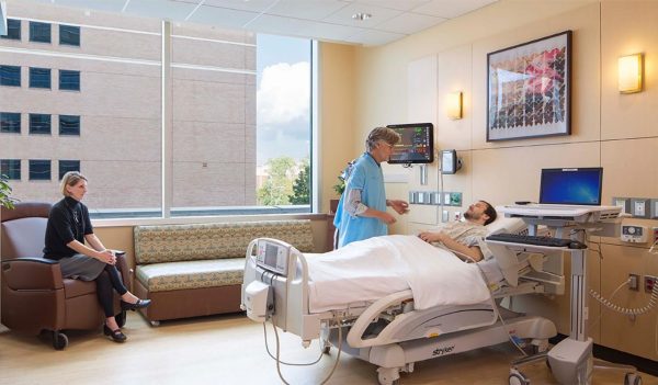 A person in a hospital bed with a nurse and visitor