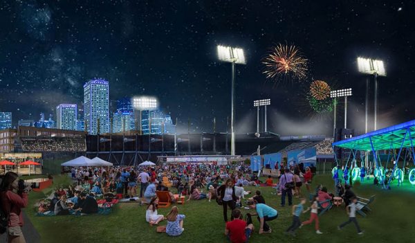 People in a park at night with field lights and fireworks