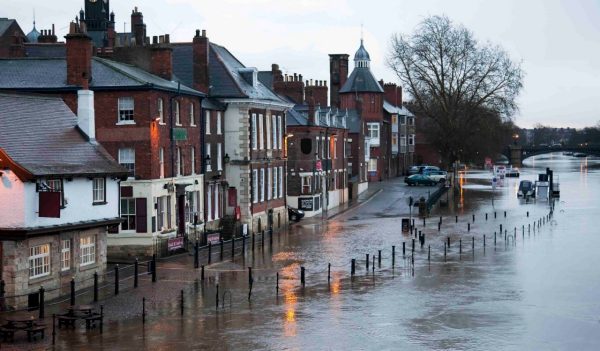 River in flood breaks its banks, covers the road and pavement, and floods the basement of the local pub. This is the River Ouse in the historic centre of York, UK.