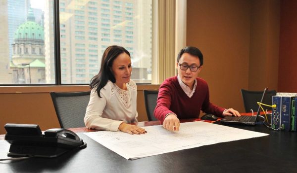 Two colleagues collaborating on plans at desk with laptop and phone.