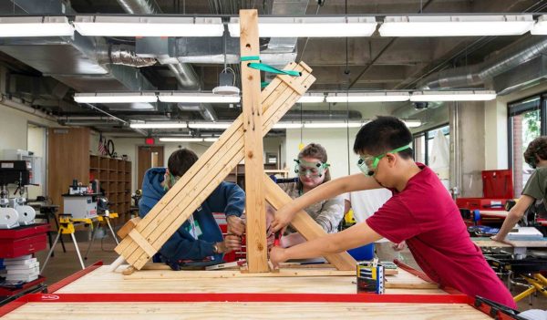 Three individuals working with wood inside a fabrication lab space.