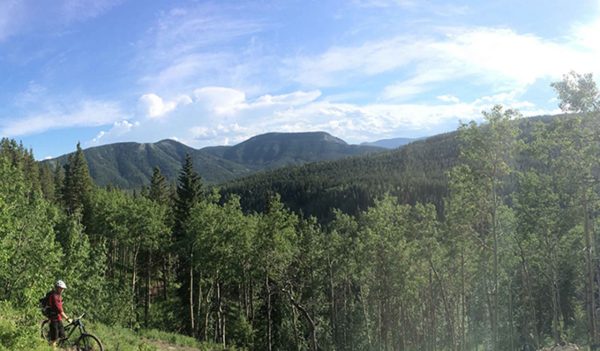 Panoramic view of Adam Baxter looking out over the green, treed hills on a Calgary bike tour.