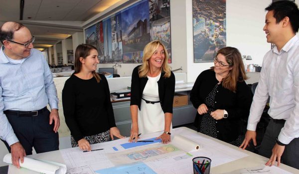 Colleagues standing around a table with design plans on it.