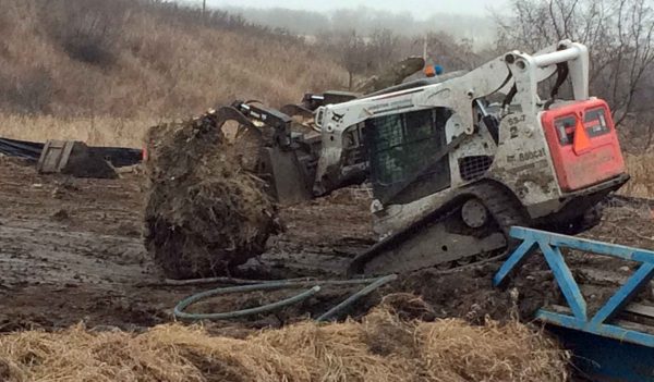 Skidsteer moving large piece of earth with forks.