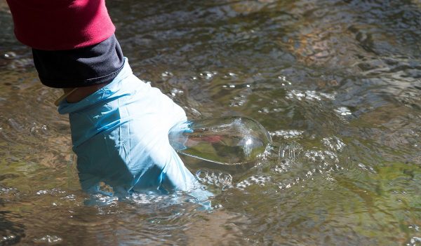 A person collecting water from a stream into a bottle