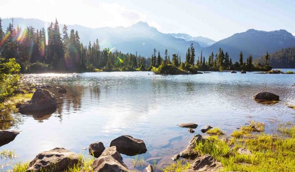 Serene scene by the mountain lake in Canada with reflection of the rocks in the calm water.