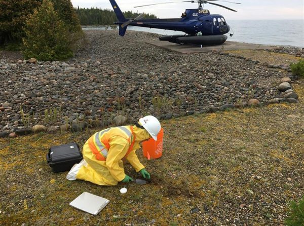 tech taking ground samples, helicopter in background