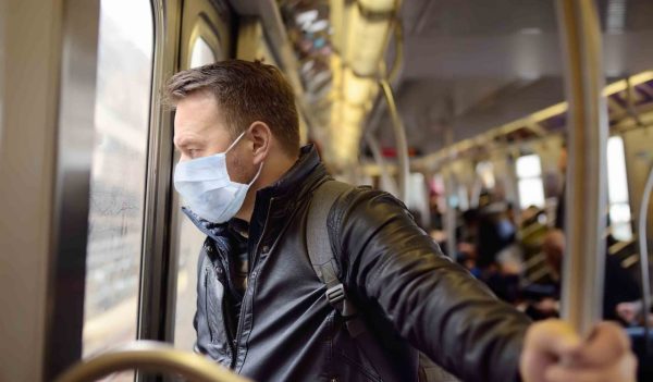 Mature man wearing disposable medical face mask in car of the subway in New York during coronavirus outbreak. Safety in a public place while epidemic of covid-19.