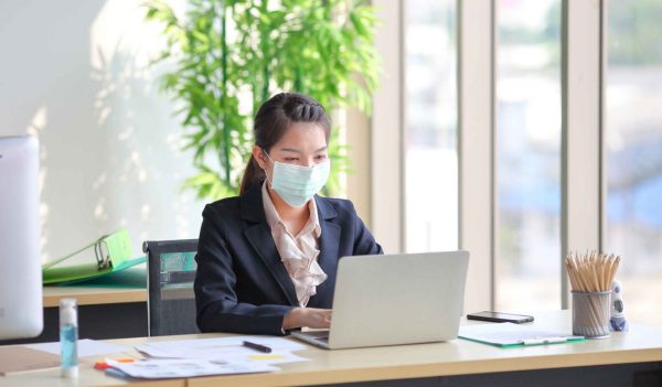 Female employee wearing medical face mask while working alone because of social distancing policy in the business office during coronavirus or covid-19 outbreak pandemic situation