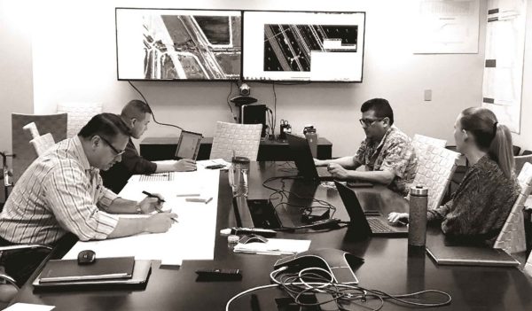  People sitting around a meeting table with drawings and computers