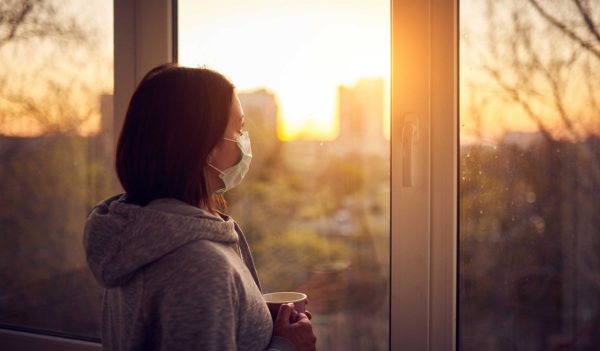 Woman near window at sunset in isolation at home for virus outbreak. Stay home concept.