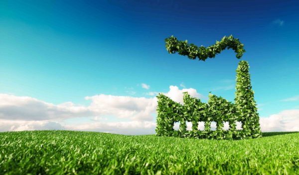 Eco friendly industry concept. 3d rendering of green factory icon on fresh spring meadow with blue sky in background.