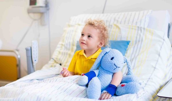 Little boy playing with his toy in bed in hospital room. Child with IV tube and pulse oximeter in modern clinic. Kid recovering from sickness. Post operative care at children station. Kids health care