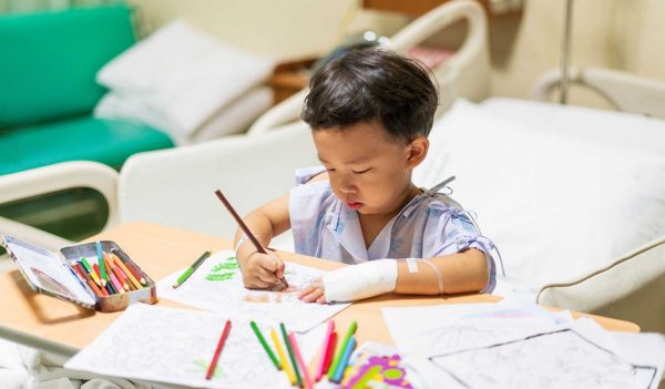 The patient boy is painting the paper with a color pencil in the hospital.