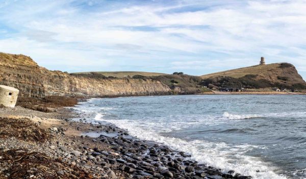 Kimmeridge Bay seascape with World War 2 pill box on sea shore and Clavell Tower on cliff top in Kimmeridge, Isle of Purbeck, Dorset, UK