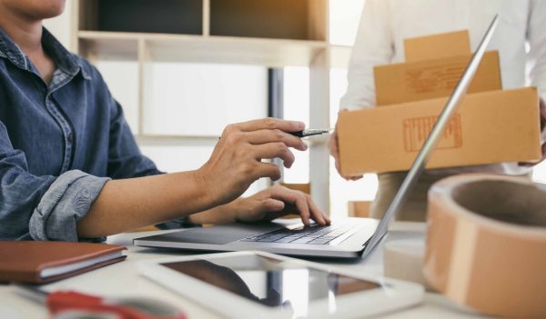 Two business owner are working together to pack products and check customers' orders on their laptops at home.