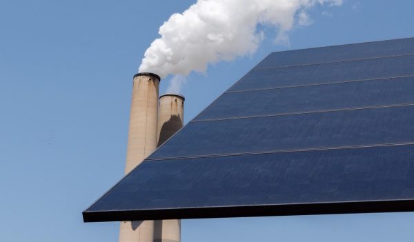 Smoking industrial chimney stack and a solar panel.