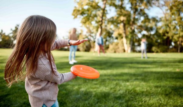 Little girl playing frisbee with her family in the park on a sunny day