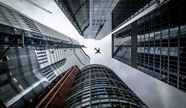 Silhouette of a jet plane flying low over Three different kind of architecture with commercial office buildings exterior in London