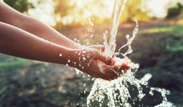 Hands outstretched with water being poured over them. 