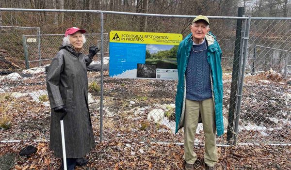 Man and woman standing in front of a fence with a sign