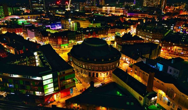 Nighttime cityscape with illuminated buildings and construction cranes, showcasing urban development in Leeds, UK.