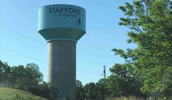 View of a tall, pedestal style, water storage tank in a rural area, surrounded by trees.