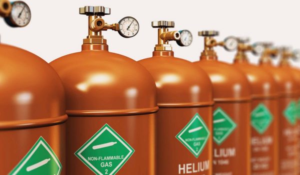 Row of orange helium tanks with green warning stickers.