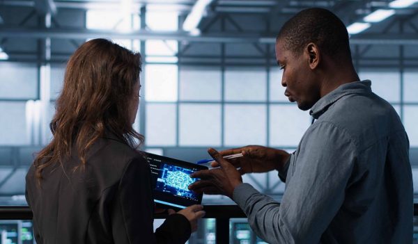 Data center system administrators using artificial intelligence neural networks tech on tablet. Teamworking server farm employees using AI programming language on device screen, camera A