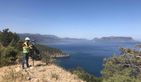 Geodetic engineer surveyor in white hard hat doing measurements with GNSS satellite receiver at the hill top above the sea