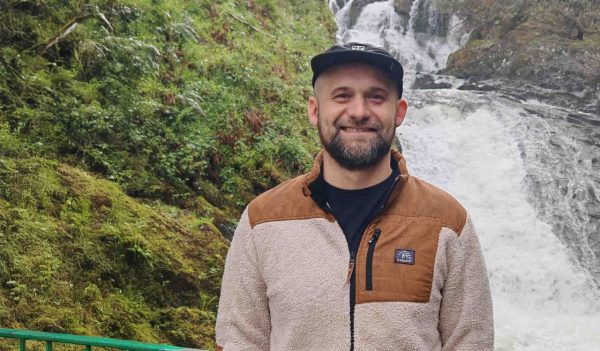 Close-up of Matthew Lange with a moss covered cliff and waterfall in the background.