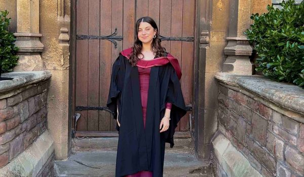 Olivia Fenwick in a graduation gown standing in front of a historial building.
