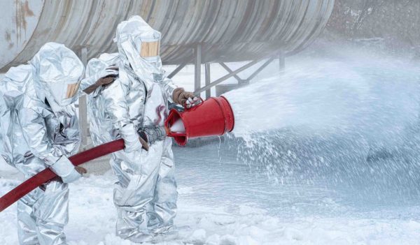 Firefighters in fire fighting operation. Airport Firefighters. Training the Firefighters. In the Foreground is a Drop of Foam Springer, a Fireman Protects Fire Safety