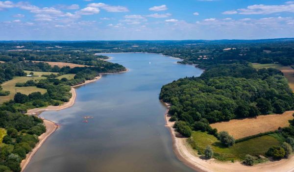 Aerial view of a reservoir surrounded by greenery on a sunny day 