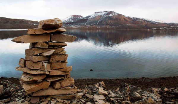 Close-up of an inukshuk with the lake and mountains in the background.