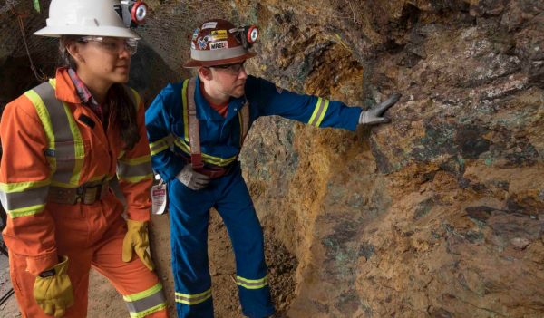 Mining employees in PPE inspecting a rock face.