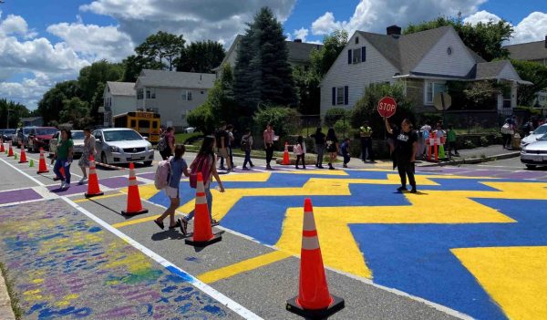 People in a crosswalk with colorful markings and a crossing guard