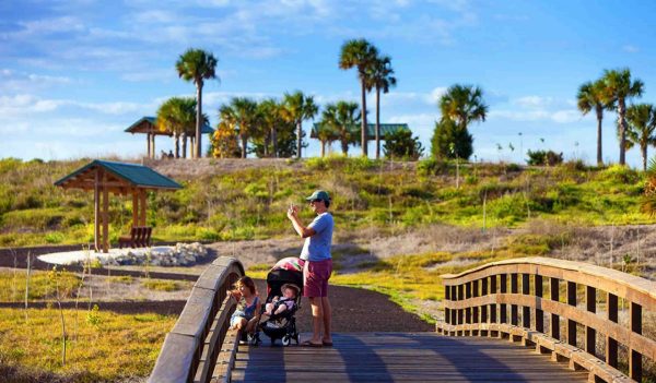 Man with a child in a stroller standing on a walking bridge.