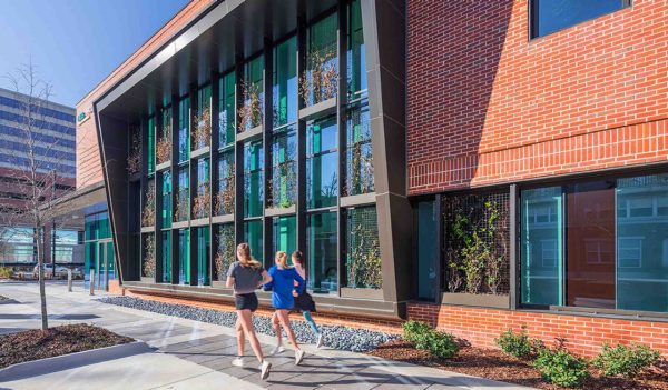 People running outside the building - brick wall with a large class feature window in the background.