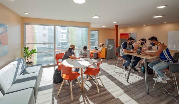 Students studying in a common area with tables and couches.