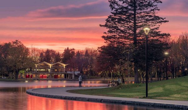 Pedestrians walking alongside the lake at dusk with a building in the background.