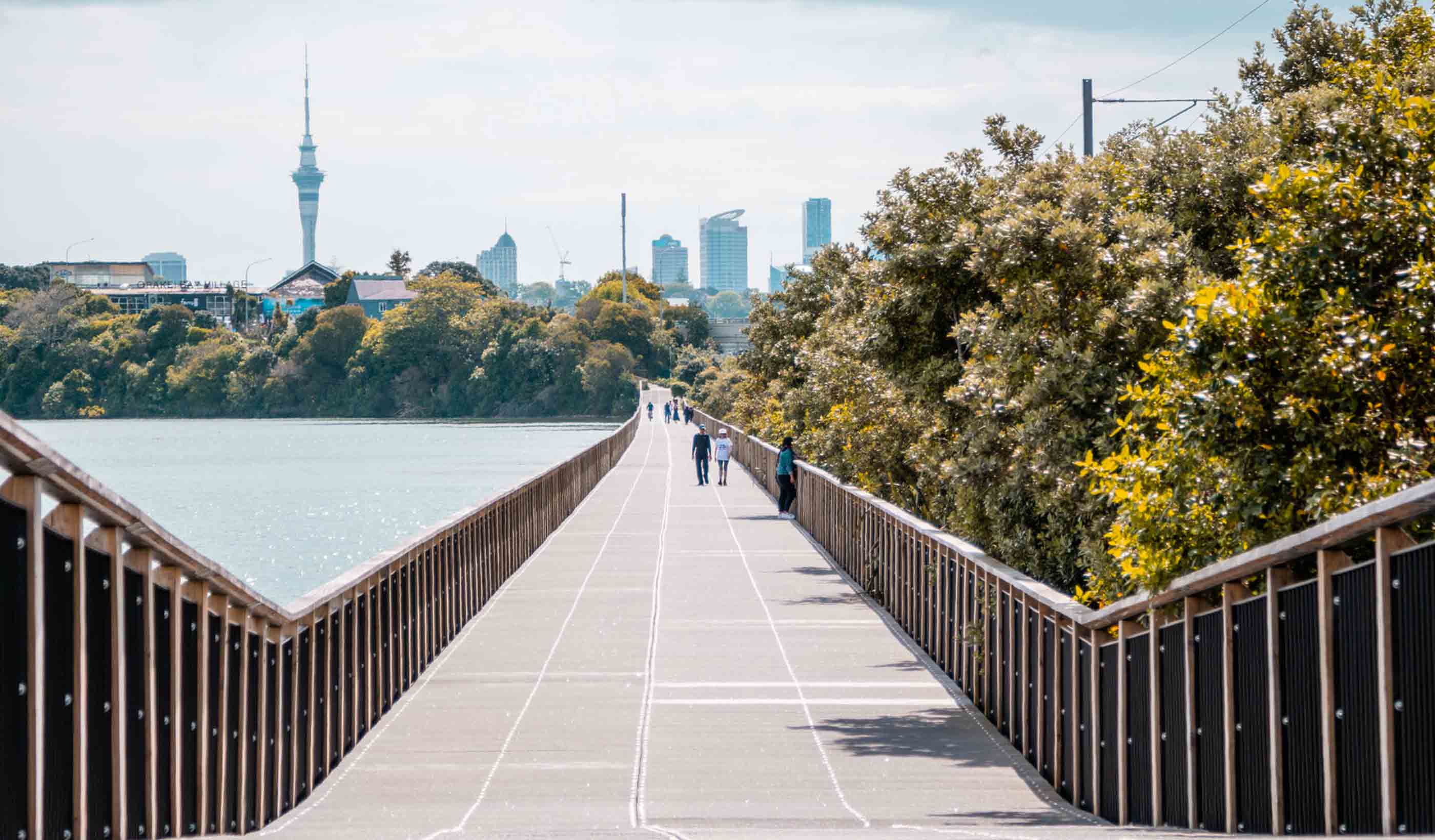 People walking across a bridge over water with the city in the background