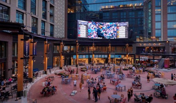 Exterior sitting area with tables and large video screen.