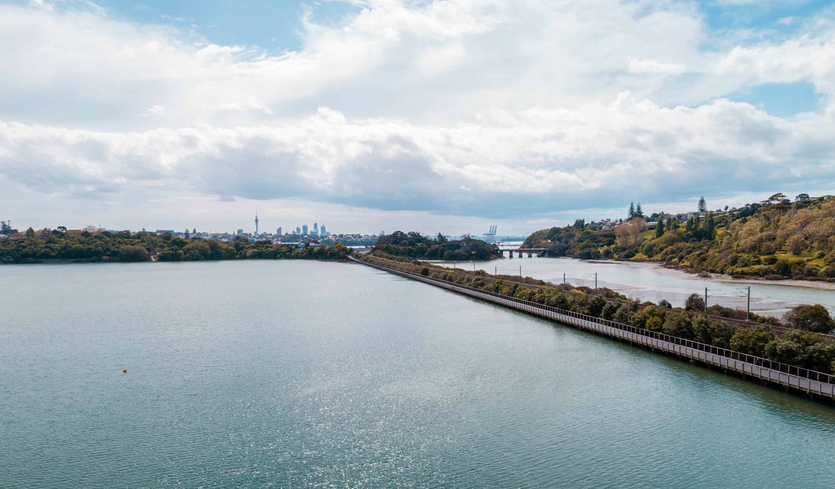 A rail line and walking path on a causeway with the city in the background