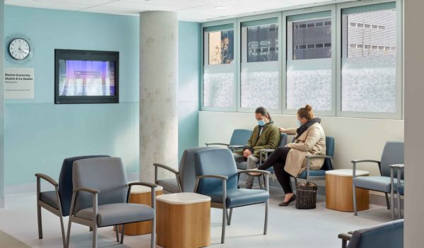 Patient waiting room in hospital with seating and side tables.