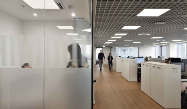 Interior open concept workstations and a private office with glass walls in neutral tones.