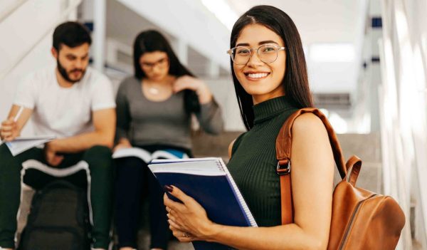 Portrait of young Brazilian student with backpack carrying books in college.