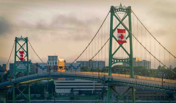 The Angus L MacDonald Bridge at dusk on Canada Day with large Canadian flags flying.