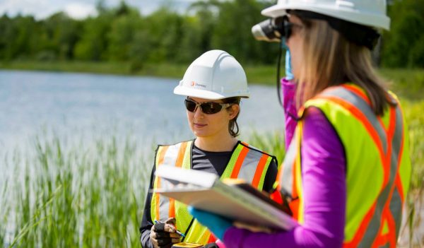 Two women conducting environmental assessments near a body of water.